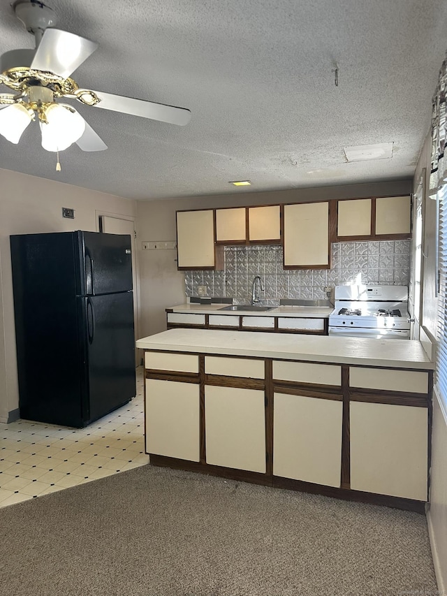 kitchen featuring a textured ceiling, white range with gas stovetop, a sink, light countertops, and freestanding refrigerator