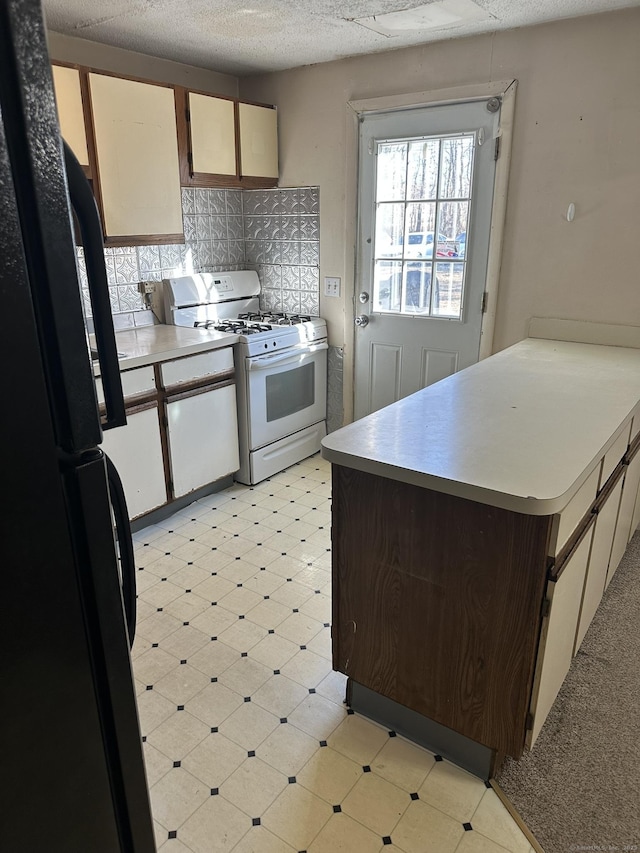 kitchen featuring tasteful backsplash, freestanding refrigerator, light countertops, white gas stove, and light floors