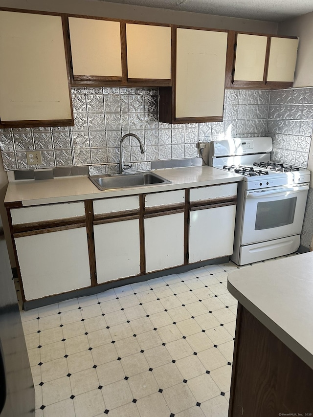 kitchen with tasteful backsplash, light countertops, white gas stove, light floors, and a sink