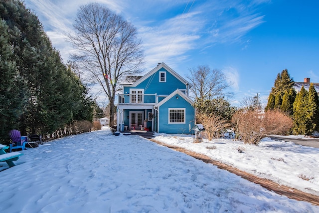 snow covered back of property featuring a balcony and french doors