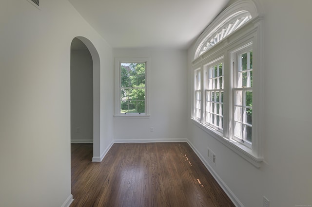 spare room with arched walkways, dark wood finished floors, visible vents, and baseboards