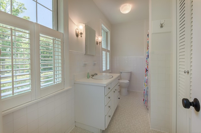 full bath with tile patterned flooring, a wainscoted wall, vanity, tile walls, and a closet