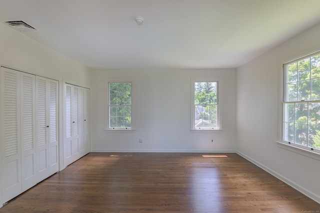 unfurnished bedroom featuring multiple windows, dark wood-style flooring, visible vents, and multiple closets