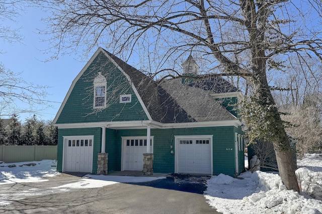 snow covered garage featuring driveway and fence