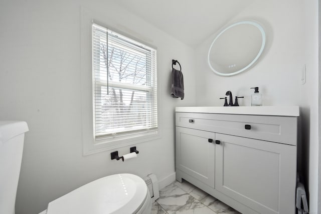 half bath with baseboards, toilet, marble finish floor, vanity, and a baseboard radiator