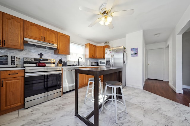 kitchen featuring marble finish floor, under cabinet range hood, a sink, appliances with stainless steel finishes, and ceiling fan