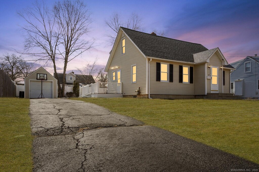 view of front of house featuring a shingled roof, a detached garage, aphalt driveway, a lawn, and an outdoor structure