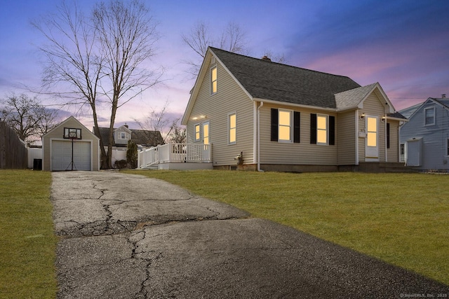 view of front of house featuring a shingled roof, a detached garage, aphalt driveway, a lawn, and an outdoor structure