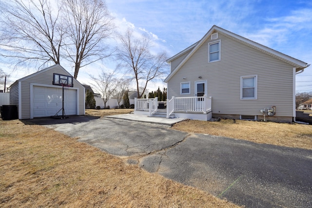 rear view of property with aphalt driveway, a detached garage, and an outbuilding