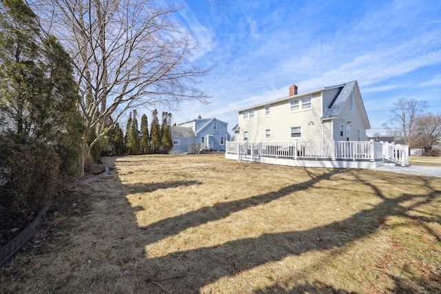 rear view of house with a lawn, a chimney, and a deck