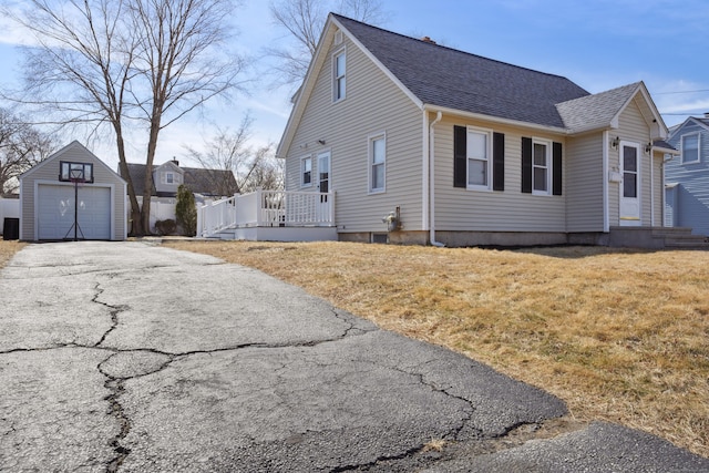 view of home's exterior featuring a shingled roof, a detached garage, a yard, an outbuilding, and driveway