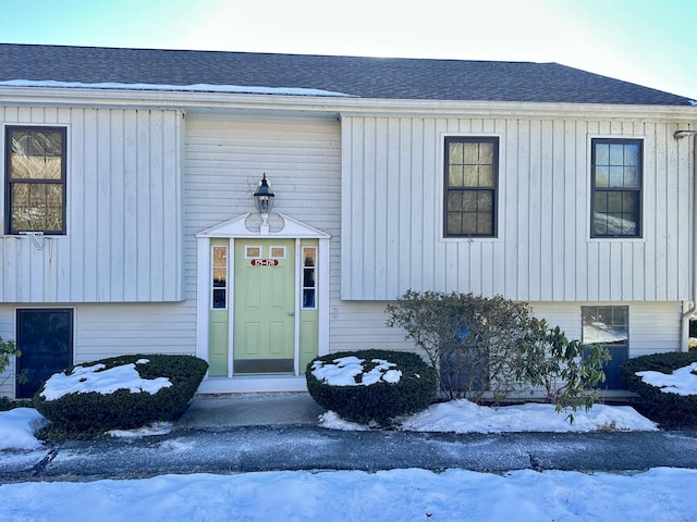 snow covered property entrance with a shingled roof