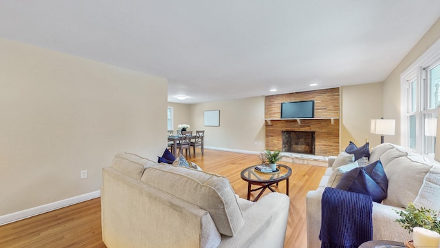 living area with baseboards, a brick fireplace, and light wood-style floors