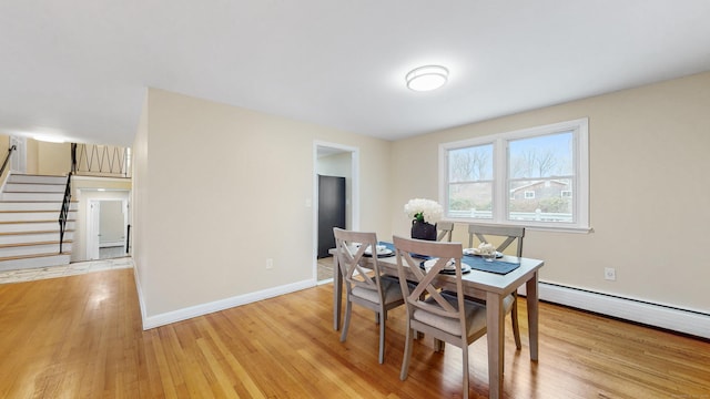 dining space with a baseboard heating unit, baseboards, stairway, and light wood finished floors