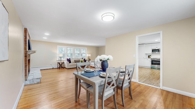 dining space with light wood-style floors, baseboards, a fireplace, and a baseboard heating unit