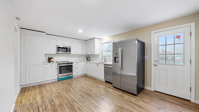 kitchen featuring light wood finished floors, white cabinetry, appliances with stainless steel finishes, and a sink