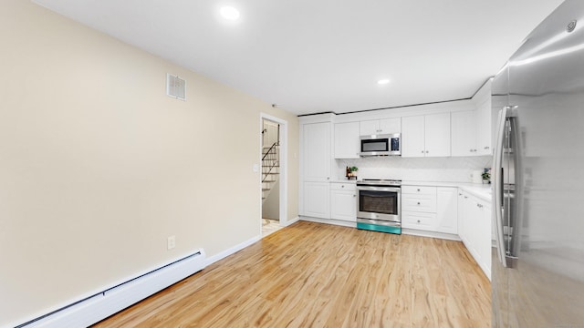 kitchen with tasteful backsplash, appliances with stainless steel finishes, a baseboard heating unit, white cabinets, and light wood-type flooring