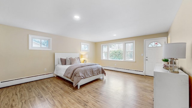 bedroom with multiple windows, baseboard heating, a baseboard radiator, and light wood-style floors