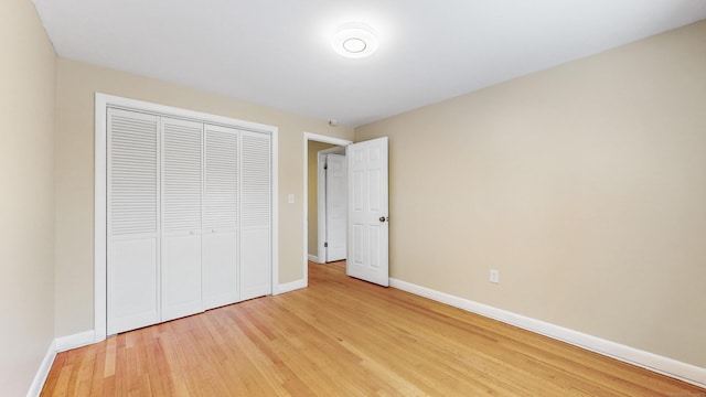 unfurnished bedroom featuring light wood-type flooring, baseboards, and a closet