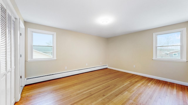 unfurnished bedroom with a baseboard heating unit, multiple windows, hardwood / wood-style flooring, and baseboards