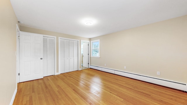 unfurnished bedroom featuring light wood-type flooring, baseboards, a baseboard heating unit, and two closets