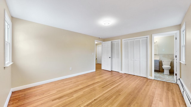 unfurnished bedroom featuring two closets, light wood-style flooring, baseboard heating, ensuite bathroom, and baseboards