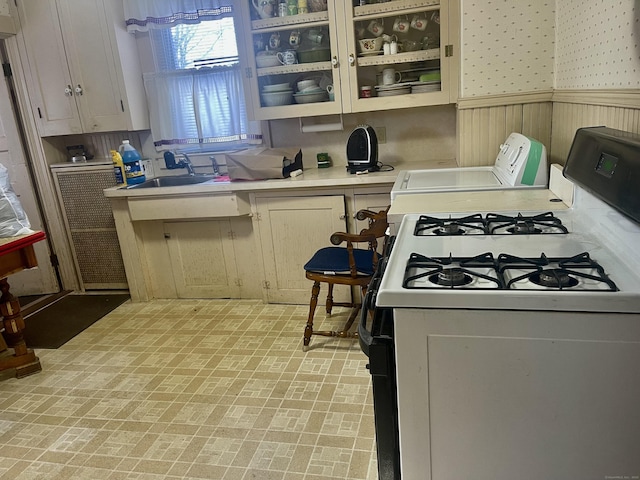 kitchen featuring a wainscoted wall, a sink, light countertops, gas range oven, and glass insert cabinets