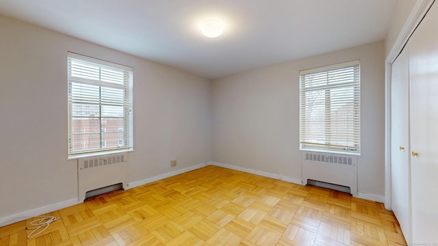 empty room with a wealth of natural light, radiator, and baseboards