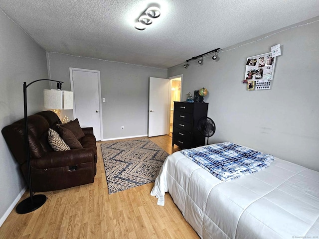 bedroom with a textured ceiling, track lighting, light wood-type flooring, and baseboards