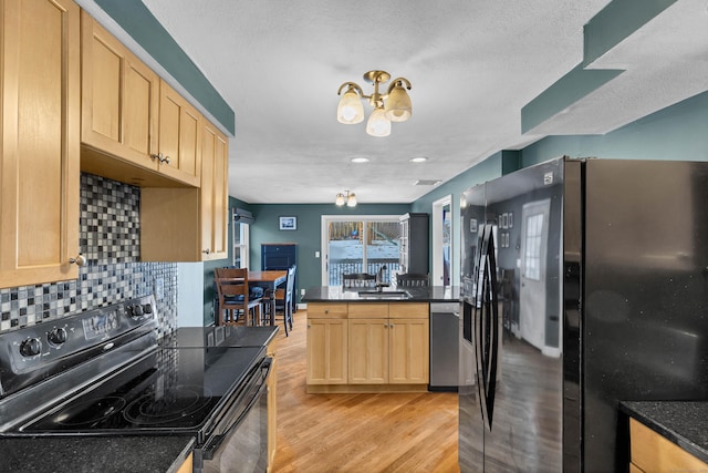 kitchen featuring dark countertops, light brown cabinetry, light wood-type flooring, black appliances, and a sink