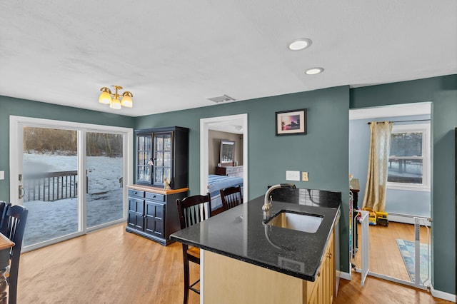 kitchen with a breakfast bar area, visible vents, light wood-style floors, a baseboard heating unit, and a sink