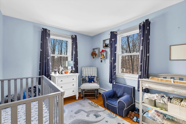 bedroom with a nursery area, multiple windows, baseboards, and wood finished floors