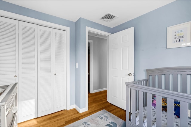 bedroom with a closet, visible vents, wood finished floors, a nursery area, and baseboards