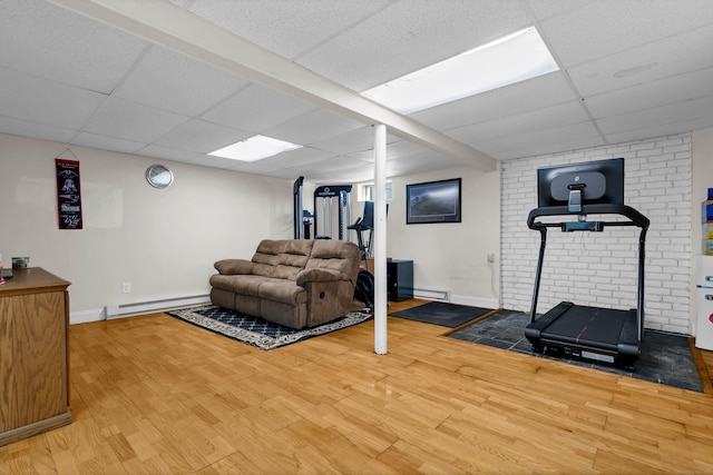 exercise area featuring a paneled ceiling, baseboards, baseboard heating, and wood finished floors