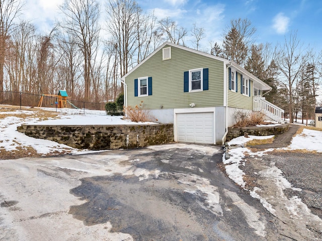 snow covered property with aphalt driveway, a playground, and an attached garage