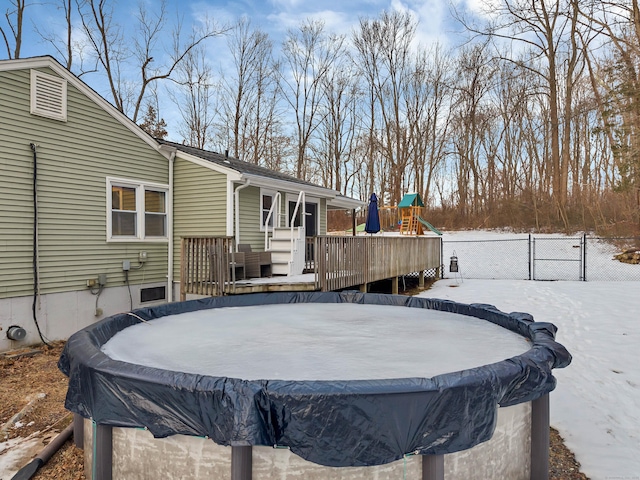 yard layered in snow with a deck, a playground, fence, and a covered pool