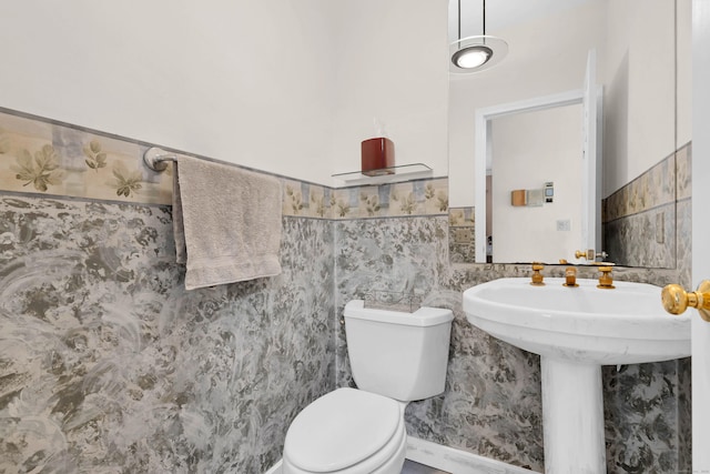 bathroom with a wainscoted wall, a sink, tile walls, and toilet