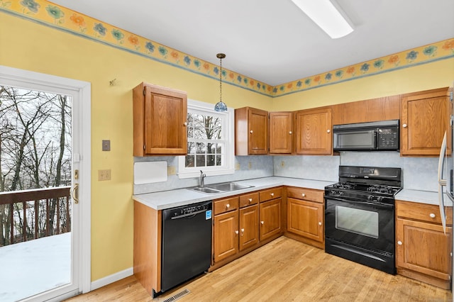 kitchen featuring a sink, light countertops, light wood-type flooring, brown cabinets, and black appliances