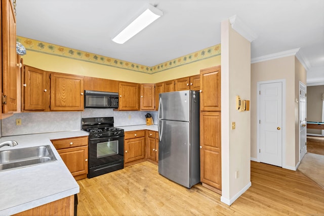 kitchen featuring light wood-style flooring, brown cabinets, light countertops, black appliances, and a sink