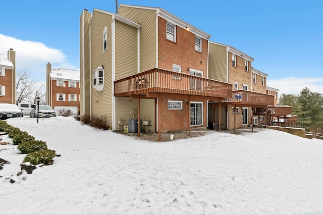 snow covered back of property featuring central AC, brick siding, and a wooden deck