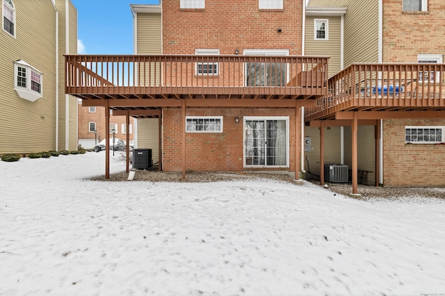 snow covered rear of property with brick siding, a wooden deck, and central AC unit