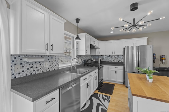 kitchen with under cabinet range hood, a sink, white cabinets, appliances with stainless steel finishes, and decorative light fixtures