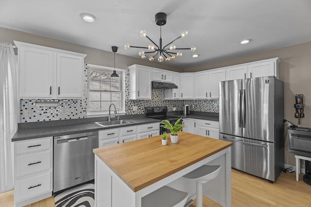 kitchen featuring under cabinet range hood, a sink, white cabinets, hanging light fixtures, and appliances with stainless steel finishes