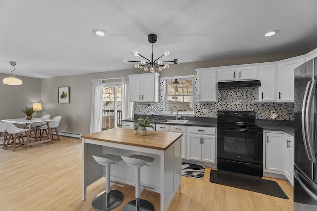 kitchen featuring under cabinet range hood, a sink, white cabinets, black electric range, and decorative light fixtures