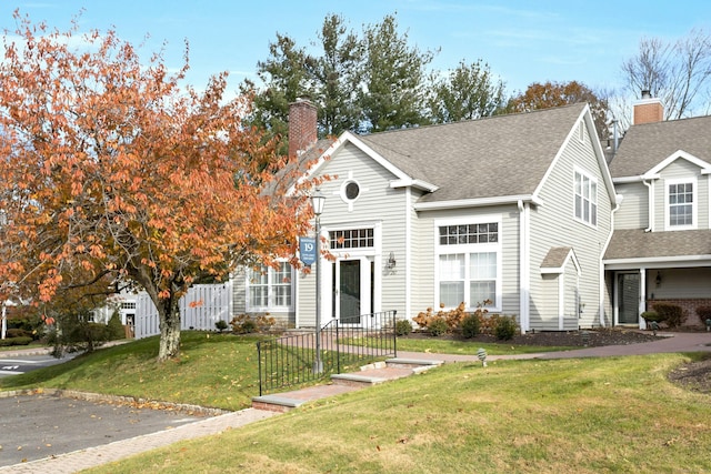 view of front of property with a shingled roof, fence, a chimney, and a front lawn