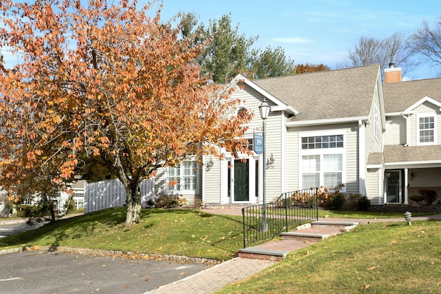 view of front facade featuring a front yard, roof with shingles, and fence