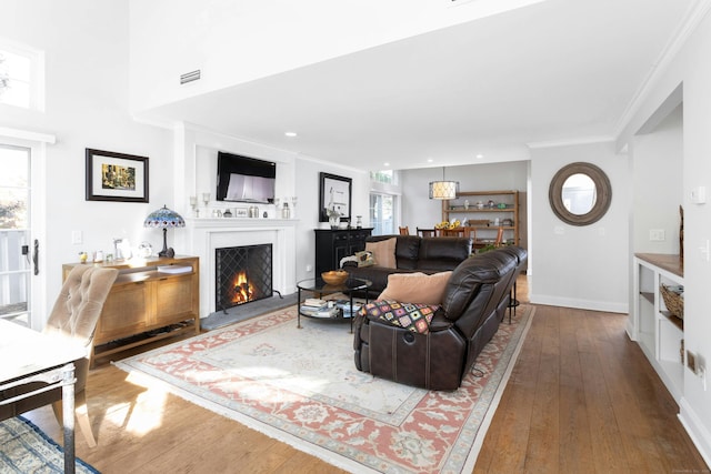 living room featuring ornamental molding, wood-type flooring, a healthy amount of sunlight, and a lit fireplace