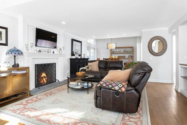 living room with baseboards, hardwood / wood-style flooring, a lit fireplace, crown molding, and recessed lighting