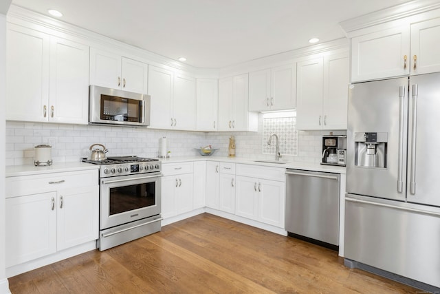 kitchen with appliances with stainless steel finishes, light countertops, light wood-type flooring, white cabinetry, and a sink