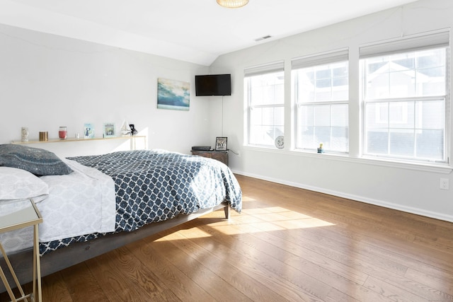 bedroom with lofted ceiling, wood finished floors, visible vents, and baseboards